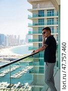 A man stands on a balcony overlooking the beautiful Dubai skyline and marina. He is casually dressed, enjoying the view while taking a phone call on a bright sunny day. Стоковое фото, фотограф Aleksandr Golubev / Фотобанк Лори