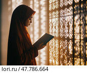Woman in a hijab praying at home, holding a misbaha, with soft light through patterned windows. Стоковое AI-изображение, AI-художник Надежда Рыбальченко / Фотобанк Лори