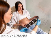 Gynecologist and pregnant woman on a couch in hospital look at an ultrasound scan of fetus. Maternity, pregnancy, fertility concept. Future mom checking on the embryo. High quality photo. Стоковое фото, фотограф Ирина Михайличенко / Фотобанк Лори