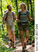 Two hikers share a joyful moment while trekking on a forest trail surrounded by greenery and warm sunlight. Стоковое AI-изображение, AI-художник Данила Большаков / Фотобанк Лори