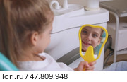Lovely little girl looking in the mirror at her teeth after teeth surgery in a pediatric stomatology. A little girl sits in a dental chair and examines her cured teeth while looking in the mirror. Стоковое видео, видеограф Ирина Михайличенко / Фотобанк Лори