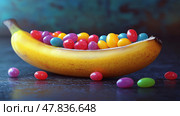 Colorful candy beans inside a banana create a fun dessert surprise. Разноцветные конфеты-бобы внутри банана - забавный десерт-сюрприз. Стоковое AI-изображение, AI-художник Katsiaryna Repich / Фотобанк Лори