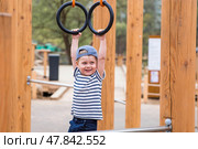 Lifestyle. A cute little boy is hanging on rings on a sports field in the fresh air. The concept of children's sports and physical development. Стоковое фото, фотограф Photojuli / Фотобанк Лори