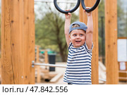 Lifestyle. A cute little boy is hanging on rings on a sports field in the fresh air. The concept of children's sports and physical development. Стоковое фото, фотограф Photojuli / Фотобанк Лори