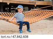 Lifestyle. A cute little boy is sitting in a hammock on a modern outdoor playground. The concept of family entertainment and leisure. Стоковое фото, фотограф Photojuli / Фотобанк Лори