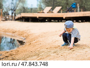 Summer lifestyle. A cute little boy is having fun playing with sand on the beach by the water. The concept of family entertainment and leisure. Стоковое фото, фотограф Photojuli / Фотобанк Лори