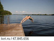 Woman in a swimsuit jumping headfirst from a pier into a lake. Capturing a powerful dive in sunlight. Стоковое фото, фотограф Скоробогатова Е. / Фотобанк Лори