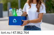A Girl in plain colors T-shirt carries a box of recyclables. Стоковое AI-изображение, AI-художник Ирина Ручушкина / Фотобанк Лори