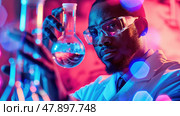 A scientist examines a beaker filled with a blue solution while surrounded by colored lights. Стоковое AI-изображение, AI-художник Данила Большаков / Фотобанк Лори