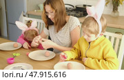 Children siblings painting Easter egg sitting together at table. Easter Family traditions. Teen girl teaching happy little brother and sister to dye, decorate eggs with paints. Preparation to holidays. Стоковое видео, видеограф Марина Демидюк / Фотобанк Лори