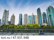 Shanghai, China - 1 April 2025: Modern Pudong business district with striking skyscrapers of diverse architecture against blue sky. A person admires the view from glass railings above lush urban park. Редакционное фото, фотограф Татьяна Терехина / Фотобанк Лори
