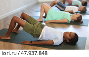 Girls and boys doing abdominal crunches with outstretched arms to strengthen abs and core muscles during group yoga class in fitness studio. Стоковое видео, видеограф Яков Филимонов / Фотобанк Лори