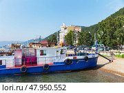 LISTVYANKA VILLAGE, IRKUTSK REGION, RUSSIA - August 03, 2023: Embankment of Lake Baikal in popular tourist village of Listvyanka. Pleasure boats and Mayak Hotel on sunny summer day. Редакционное фото, фотограф Виктория Катьянова / Фотобанк Лори