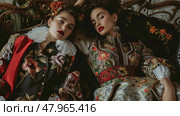 Two models with elaborate makeup are posing in ornate floral dresses, exuding an air of classical fashion elegance. Стоковое AI-изображение, AI-художник Данила Большаков / Фотобанк Лори