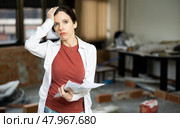 Puzzled woman examining house during renovation, comparing with blueprints. Стоковое фото, фотограф Яков Филимонов / Фотобанк Лори
