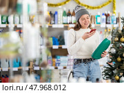 In Christmas decorated shop, girl client scanning QR code on package laundry fabric softener. Стоковое фото, фотограф Яков Филимонов / Фотобанк Лори