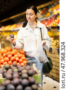 Woman carefully selects fresh tomatoes, standing near the counter in supermarket. Стоковое фото, фотограф Яков Филимонов / Фотобанк Лори