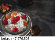 An easy healthy breakfast. A bowl filled with grainy, creamy cottage cheese is decorated with bright yellow and red raspberries. The dish stands on a dark textured surface. Copy space. Стоковое фото, фотограф Оксана Медведева / Фотобанк Лори