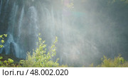 Waterfall mist rises high in forest air as water cascades down rocky green cliff face. Стоковое видео, видеограф Ольга Сухарева / Фотобанк Лори