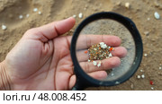 Hand holding a magnifying glass over a pile of sand. Microplastic. Стоковое AI-изображение, AI-художник Sergey Grishin / Фотобанк Лори