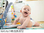 Улыбающийся малыш лежит на животе на развивающем коврике с дугами, на дугах висят мягкие игрушки. Младенцу 4 месяца. Стоковое фото, фотограф Яна Проничева / Фотобанк Лори