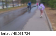 Blurred image: A child riding a scooter in a park surrounded by moving people. Стоковое видео, видеограф Zakharova Natasha / Фотобанк Лори