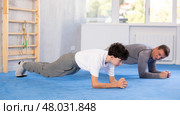 Underage boy and middle-aged trainer practicing plank pose in sports hall. Стоковое фото, фотограф Яков Филимонов / Фотобанк Лори