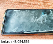 Cracked smartphone screen on wooden table showing signs of damage and wear. Стоковое фото, фотограф Кривошеина Елена Леонидовна / Фотобанк Лори