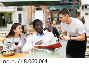 In the open area of the cafe, good fighter communicates with a multinational couple of visitors, accepts an order. Стоковое фото, фотограф Яков Филимонов / Фотобанк Лори