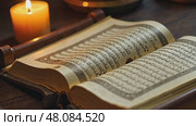 A close-up of a dusty Qur'an resting on a wooden stand, Koran pages open to a verse about sacrifice, bathed in soft candlelight. Стоковое AI-видео, аниматор Sergey Grishin / Фотобанк Лори
