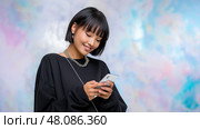 Young Asian Woman with Sleek Bob Scrolling Smartphone with excitement. Молодая женщина азиатского происхождения с гладкой черной стрижкой боб, с увлечением читает на своем смартфоне, на фоне яркого цифрового фона. Стоковое AI-изображение, AI-художник Katsiaryna Repich / Фотобанк Лори