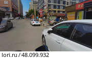 Guangzhou, China - July 12, 2024: A lively urban street scene that features parked cars alongside diverse shops and storefronts. Редакционное фото, фотограф David Kashakhi / Фотобанк Лори