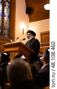Rabbi speaking from wooden podium to congregation in synagogue. Стоковое AI-изображение, AI-художник Юрий Поздников / Фотобанк Лори