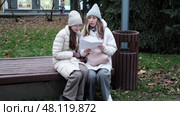 Mother and daughter in the city. Relaxed woman and daughter going to autumn street, sitting on a park bench. Teen girl student wear warm clothes winter jacket. Teenager out for walk with mom. 4K. Стоковое видео, видеограф Марина Демидюк / Фотобанк Лори