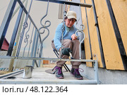 Purposeful painting of metal railing with black paint is carried out by woman to preserve structure and improve appearance of rural house entrance. Стоковое фото, фотограф Владимир Григорьев / Фотобанк Лори