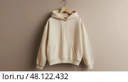 Neutral cream hoodie  hanging on a hanger against a plain background. Нейтральная кремовая толстовка висит на вешалке на однотонном фоне. Стоковое AI-изображение, AI-художник Katsiaryna Repich / Фотобанк Лори