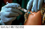 A healthcare professional wearing gloves injects a vaccine into a person’s arm, seen in a well-lit medical environment. Стоковое AI-изображение, AI-художник Данила Большаков / Фотобанк Лори