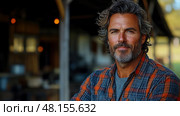 A confident man with a beard wears a flannel shirt in a rustic barn, capturing the essence of outdoor living during the golden hour. Стоковое AI-изображение, AI-художник Данила Большаков / Фотобанк Лори