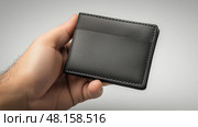 Strong hand holding a sleek black wallet in a minimalist setting. мужская рука держит элегантный черный бумажник в минималистическом стиле. Стоковое AI-изображение, AI-художник Katsiaryna Repich / Фотобанк Лори