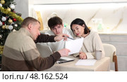 Male realtor discusses the terms of contract with couple in office of real estate agency, offering various accommodation options against backdrop of a Christmas tree. Стоковое видео, видеограф Яков Филимонов / Фотобанк Лори