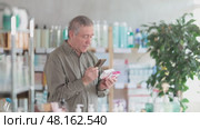 Thoughtful casually dressed elderly man using smartphone to scan barcode on paracetamol box at pharmacy, looking for pain or fever relief information before purchase. Стоковое видео, видеограф Яков Филимонов / Фотобанк Лори