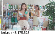 Confused young woman in summer outfit standing in busy supermarket, holding bottle of shampoo and touching hair with concerned expression, pondering right choice for hair care routine. Стоковое видео, видеограф Яков Филимонов / Фотобанк Лори