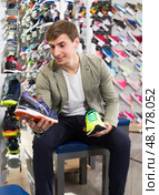 Young man compares two pairs of sneakers in a store. Стоковое фото, фотограф Татьяна Яцевич / Фотобанк Лори