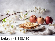 Jewish matzo bread with flowering twigs and apples on a white background. The concept of the Passover holiday. Стоковое AI-изображение, AI-художник Данила Большаков / Фотобанк Лори