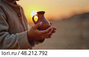 A child's small hands holding a clay water jug, symbolizing the thirst of Imam Hussain's family, under the fading light of sun. Стоковое AI-видео, аниматор Sergey Grishin / Фотобанк Лори