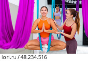 Girl doing Baddha Konasana asana in hammock under supervision of female coach. Стоковое фото, фотограф Яков Филимонов / Фотобанк Лори