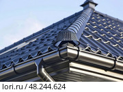 A close up view of a black metal roof with rain gutters on a sunny day. Стоковое AI-изображение, AI-художник Данила Большаков / Фотобанк Лори
