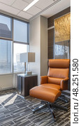 A tan leather office chair with a black swivel base sits in a modern office. Стоковое AI-изображение, AI-художник Данила Большаков / Фотобанк Лори