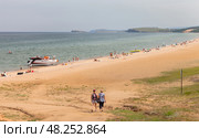 BAIKAL LAKE, OLKHON ISLAND, KHUZHIR VILLAGE, IRKUTSK REGION, RUSSIA - August 03, 2024: People and tourists relax and sunbathe on the sandy beach of Saraiskiy Bay on a summer sunny day. Редакционное фото, фотограф Виктория Катьянова / Фотобанк Лори