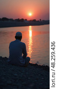 A Lone Mourner by the River at Twilight Whispers Prayers for Martyrs, Reflecting on Healing and Remembrance. Стоковое AI-изображение, AI-художник Sergey Grishin / Фотобанк Лори